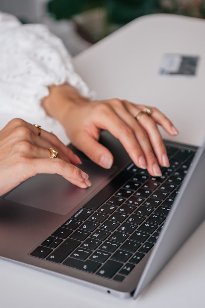 about-01 Hands of a woman typing on a laptop keyboard indoors, showcasing rings and fashion.